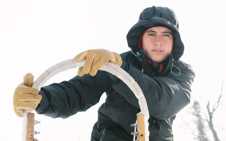 a person wearing snow gear holds the handles of a sled and looks at the camera
